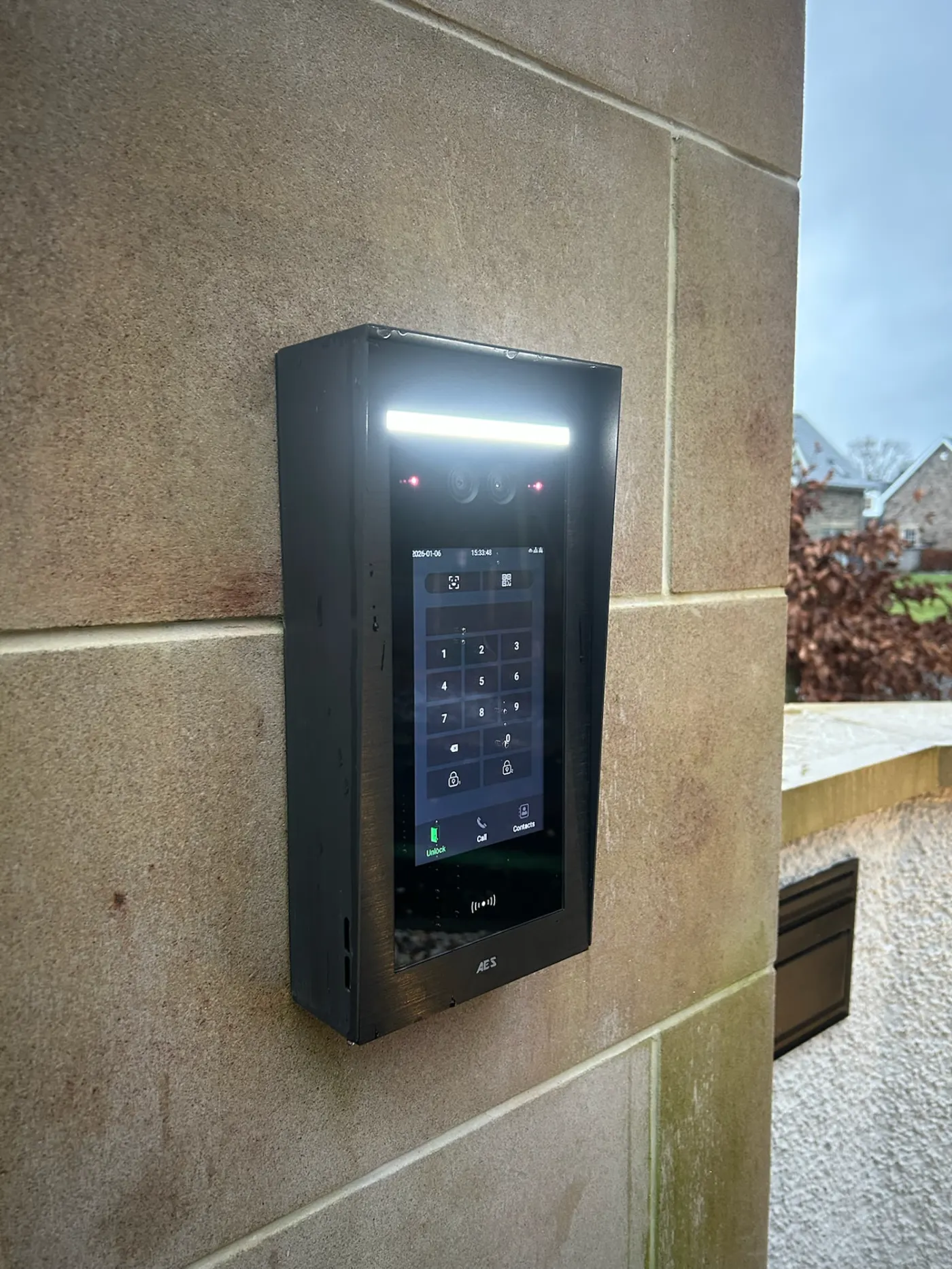 AES Global Ltd touchscreen video intercom keypad installed on a stone wall by KLR Design Limited