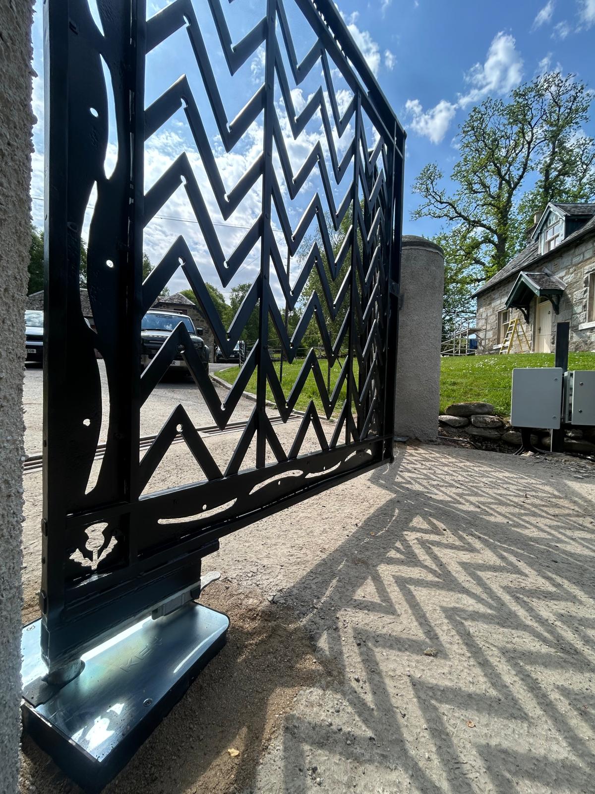 Angled view of the bespoke chevron wrought-iron-style swing gate with Scottish thistle detail and KEY underground motor at Edinample Castle by KLR Design