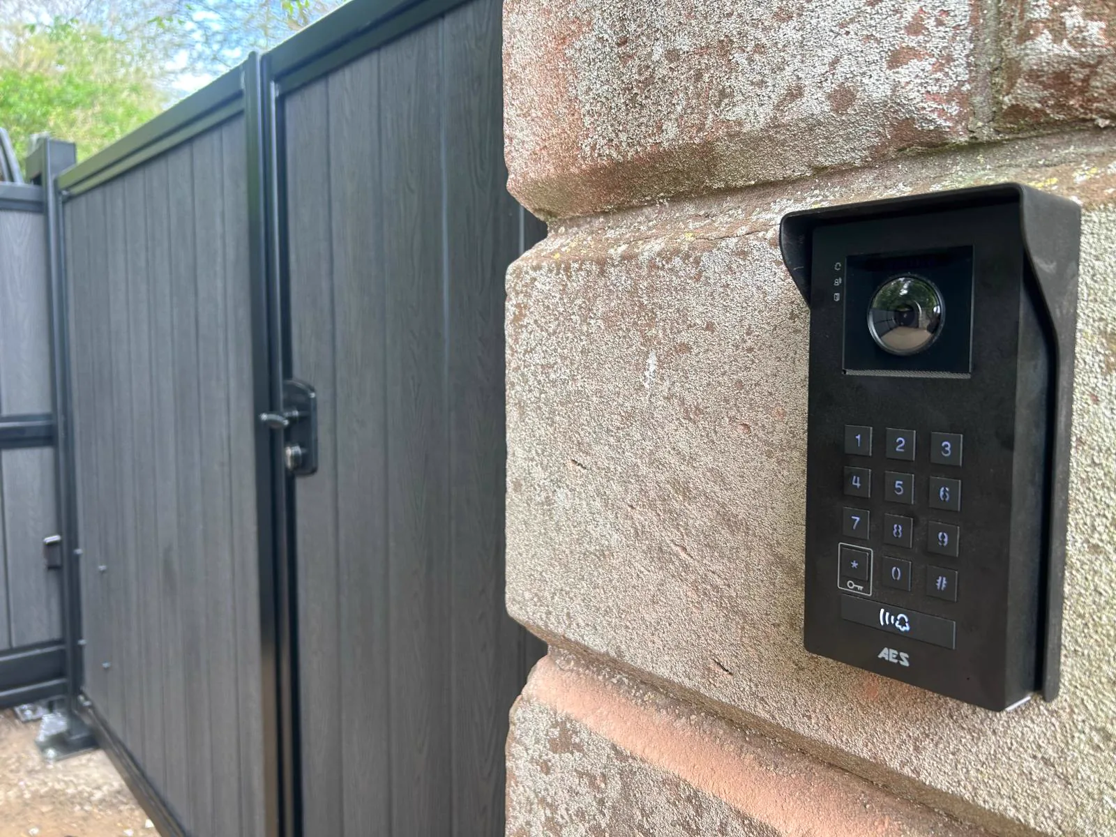 Composite sliding gate with AES Global video intercom installed on a stone pillar by KLR Design Limited
